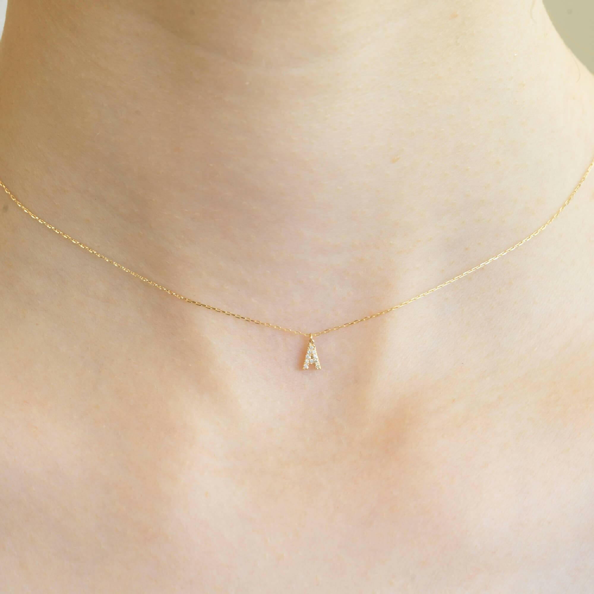 胸元で輝く10KゴールドAイニシャルネックレス(ダイヤ付きチャーム)を着用した女性モデルのアップ