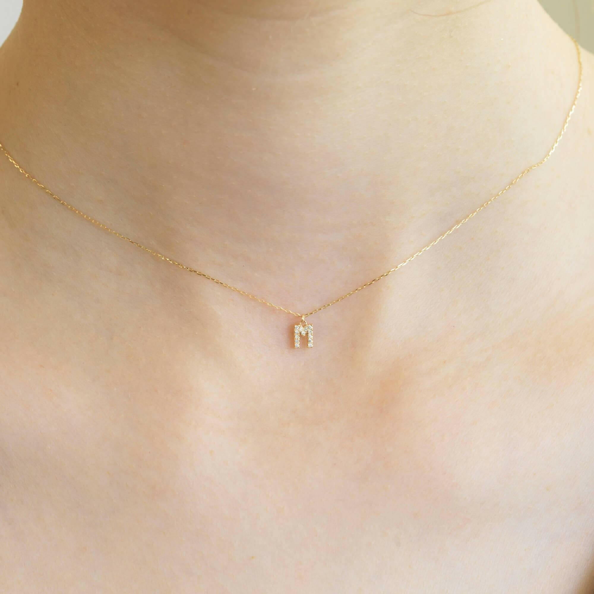 胸元で輝く10KゴールドMイニシャルネックレス(ダイヤ付きチャーム)を着用した女性モデルのアップ