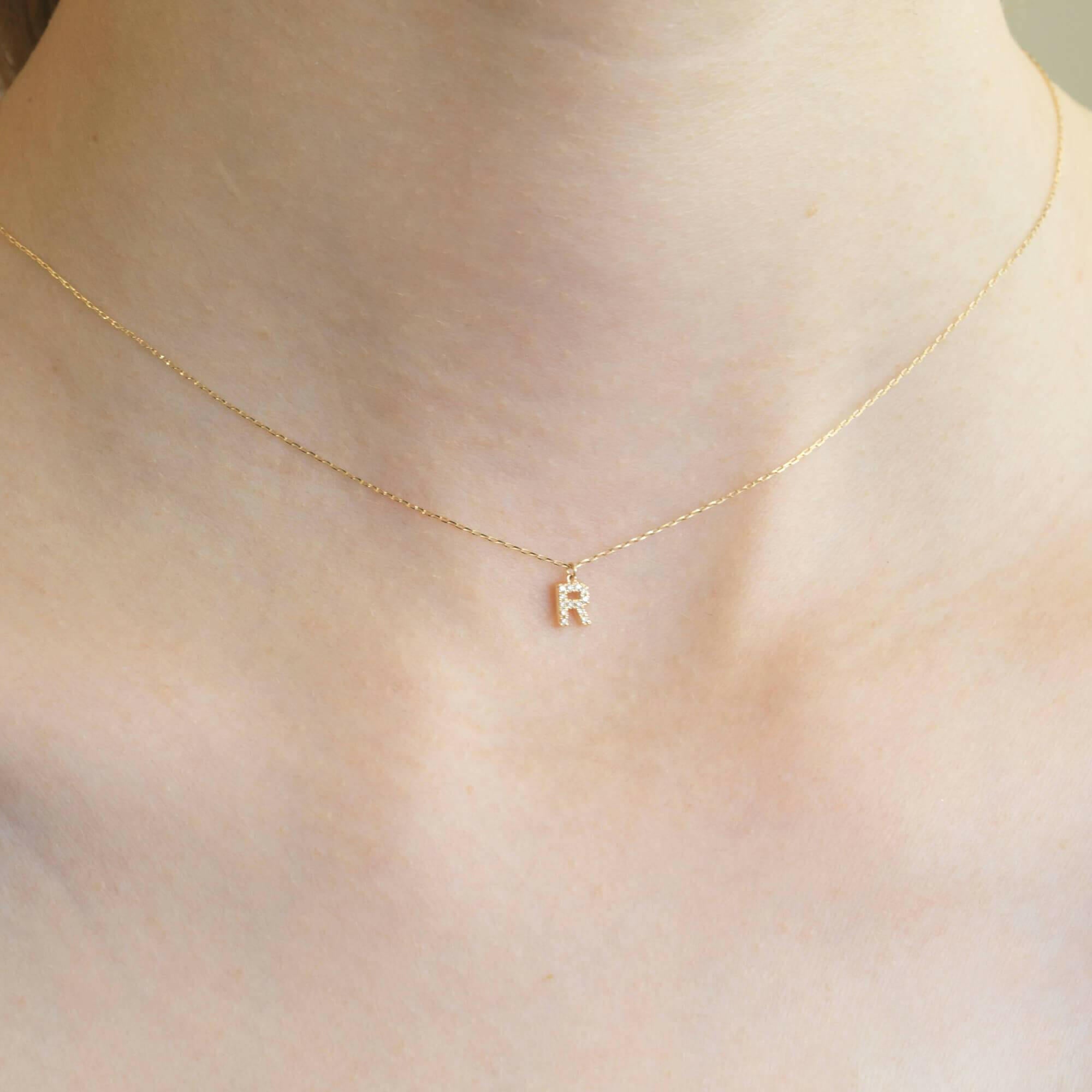 胸元で輝く10KゴールドRイニシャルネックレス(ダイヤ付きチャーム)を着用した女性モデルのアップ