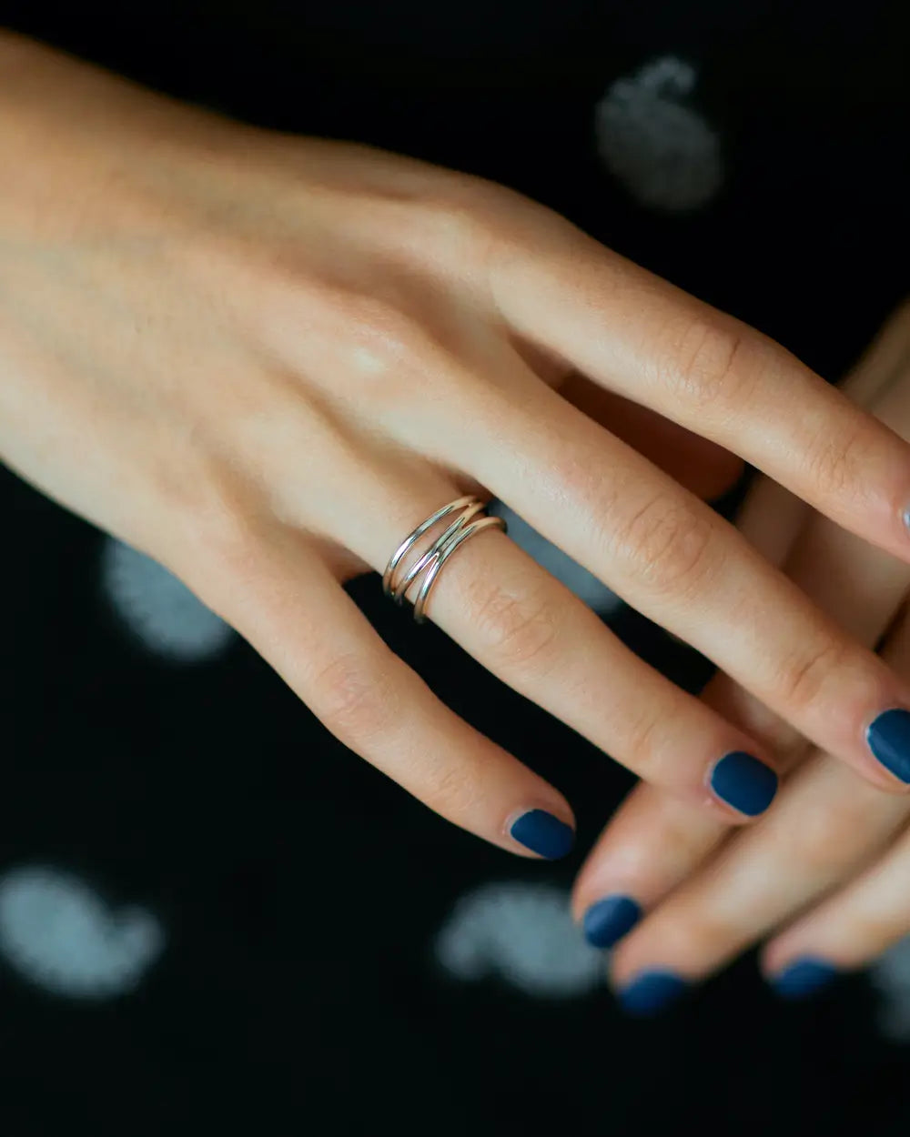 黒のトップスに合わせたシルバーの3連風ウェーブリング。洗練された手元のスタイリング例。