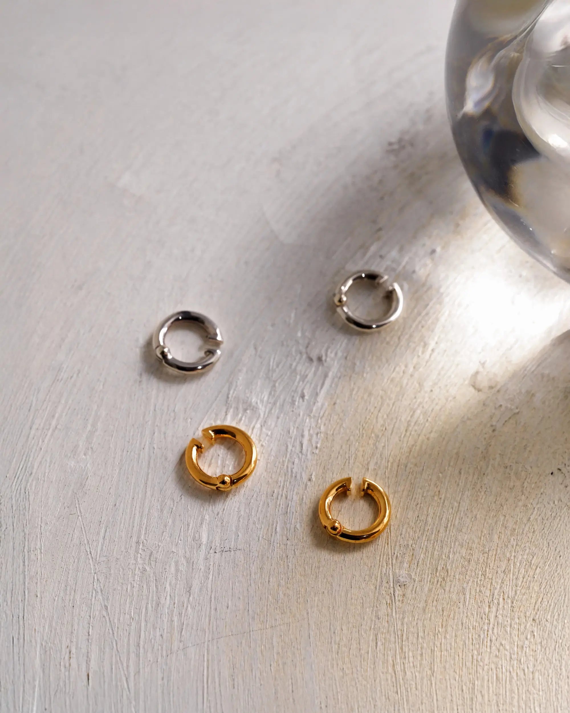 ガラスのオブジェと並ぶクラシックフープイヤリング(ゴールド・シルバー)の商品画像。引き算の美学から生まれたミニマルなフォルム。