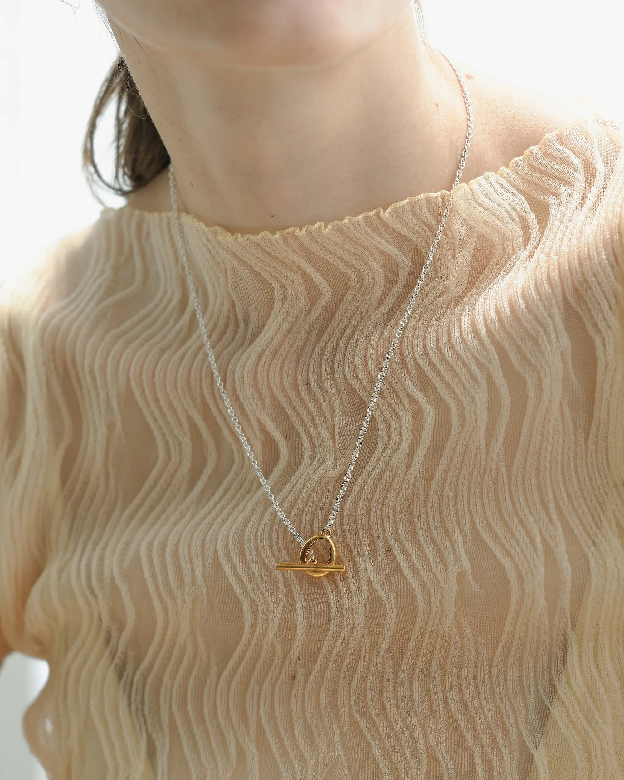 デュードロップネックレス バイカラー アップ | ゴールドのマンテルパーツが胸元で華やかに輝く