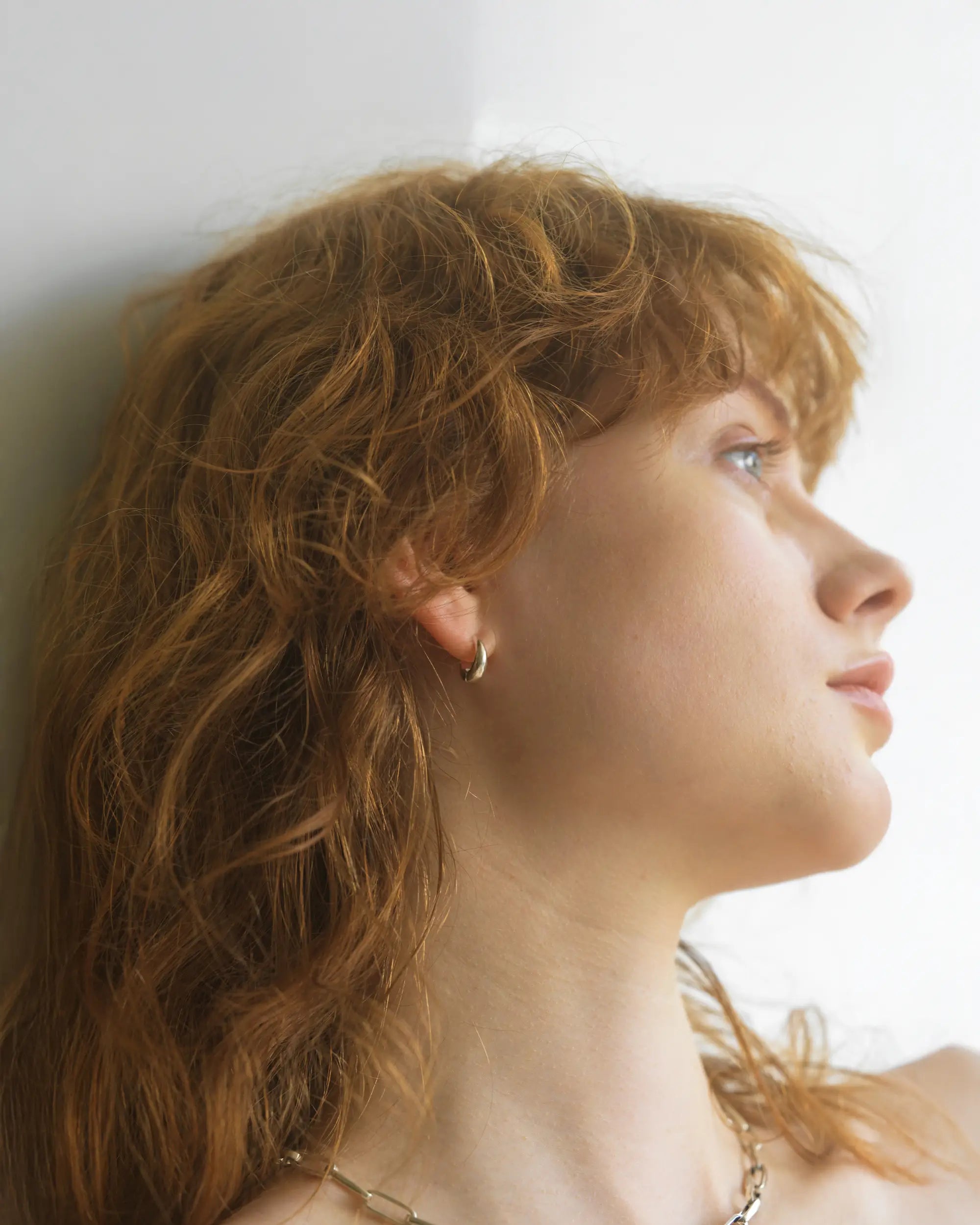 暗がりの背景に浮かび上がる、痛くなりにくいバネ式イヤリングを着用した大人の女性の美しい横顔。