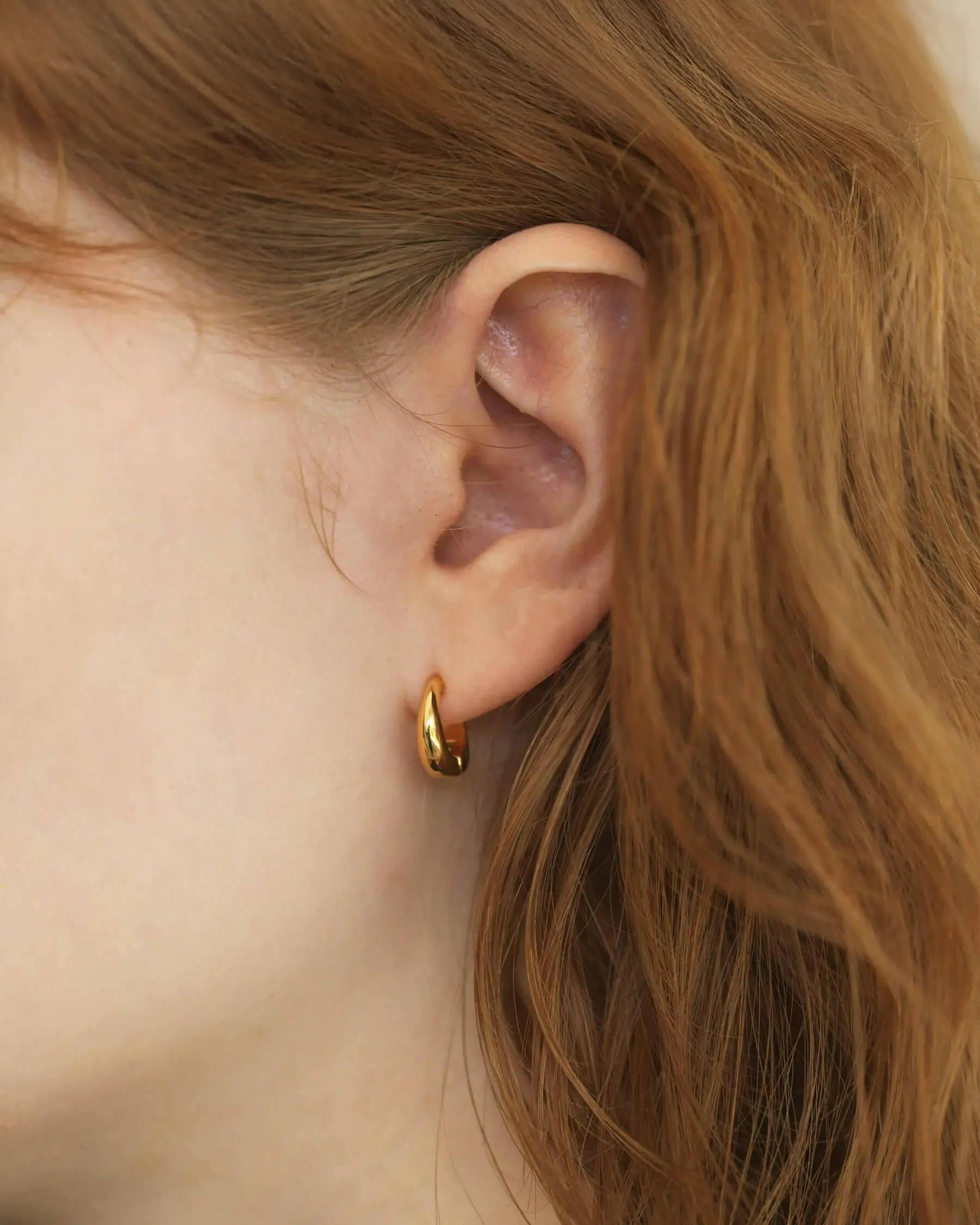 約5mmの厚みがもたらす立体的な陰影が美しい、ゴールドのバネ式フープイヤリングを着用した右耳のアップ。