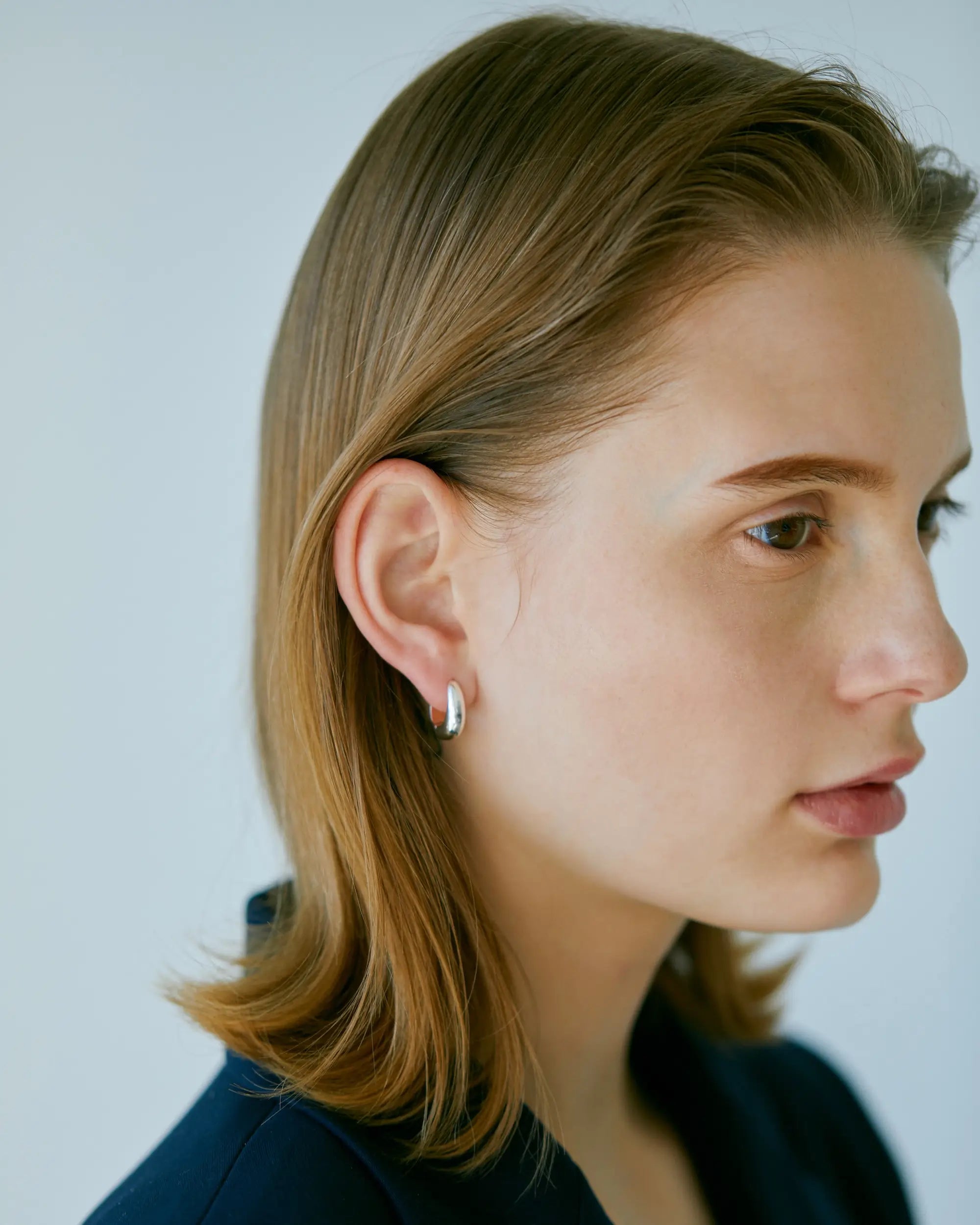シルバーのヒンジドフープピアスを着用した女性の横顔。有機的な曲線と人工的な造形を一つに結んだ美しいフォルム。