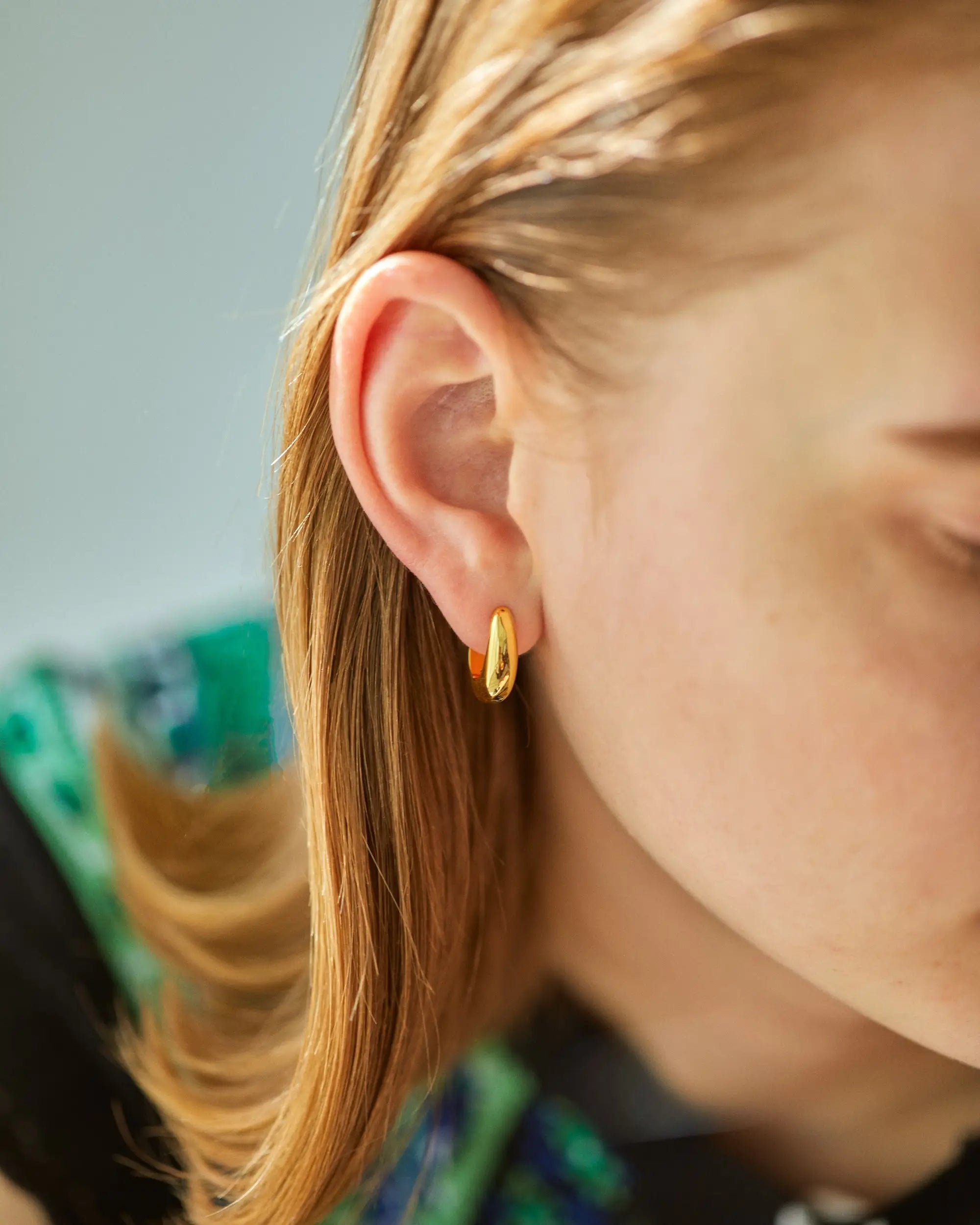 ゴールドのヒンジドフープピアスを着用した女性の横顔。控えめさと大胆さを併せ持つ、洗練された造形。