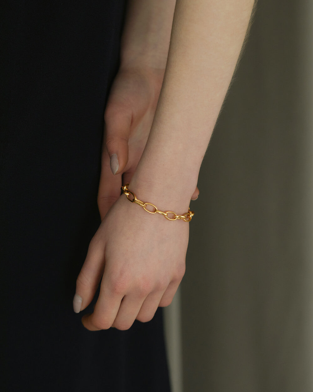 オーバルチェーンブレスレット ゴールド 手元 | シンプルな黒トップスを引き立てる大人のボリュームブレス