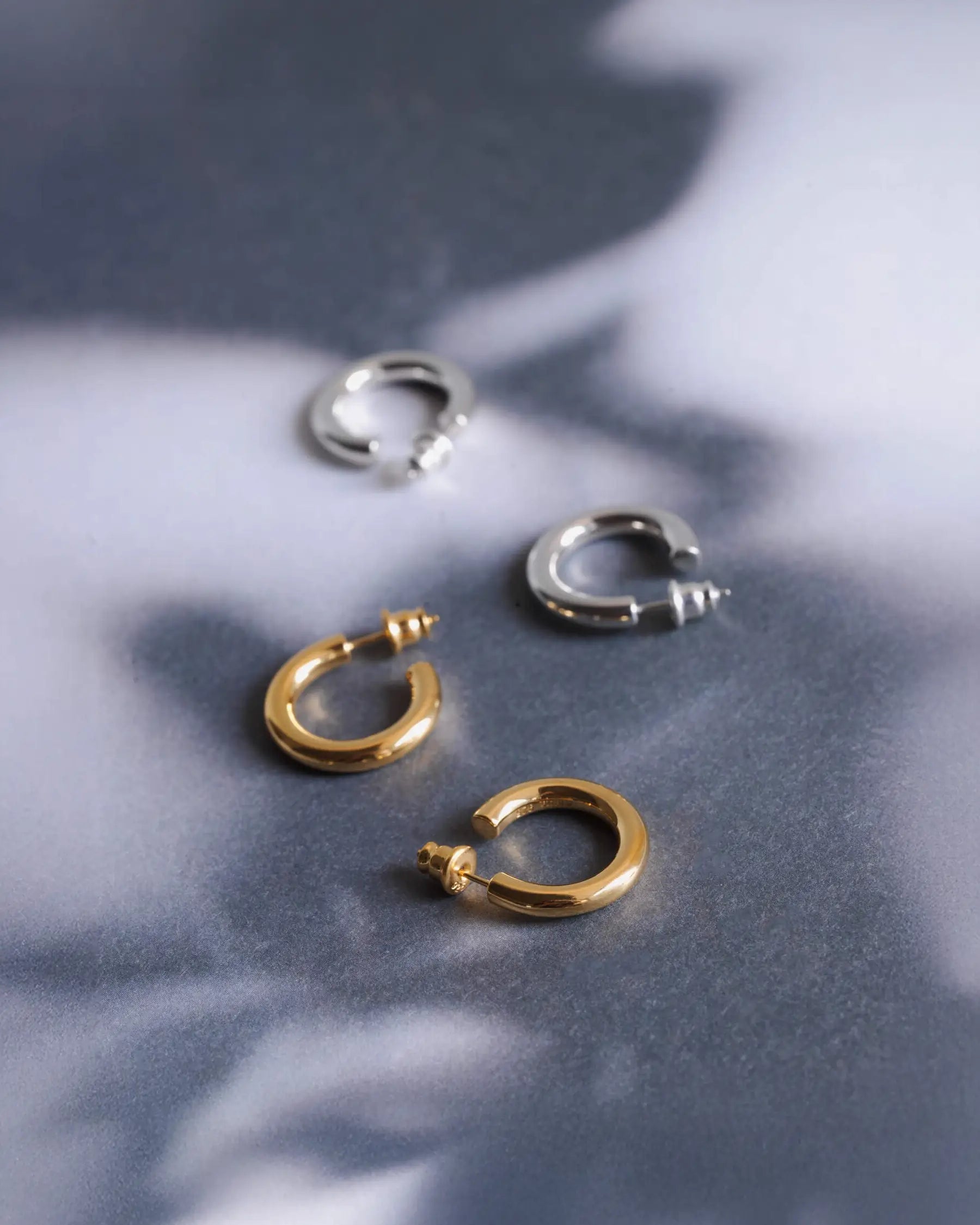 美しい影を落とすオーバルフープピアス M(シルバー・ゴールド)の置き画。クラシックな美しさをモダンに再構築したタイムレスなアクセサリー。