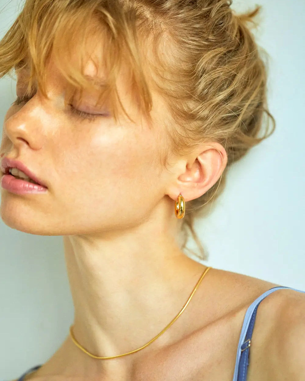 プランプフープピアス(ゴールド)を着用して上を向くモデル。厚み約4mmのぷっくりとしたフォルムが耳元に柔らかなニュアンスをプラス。