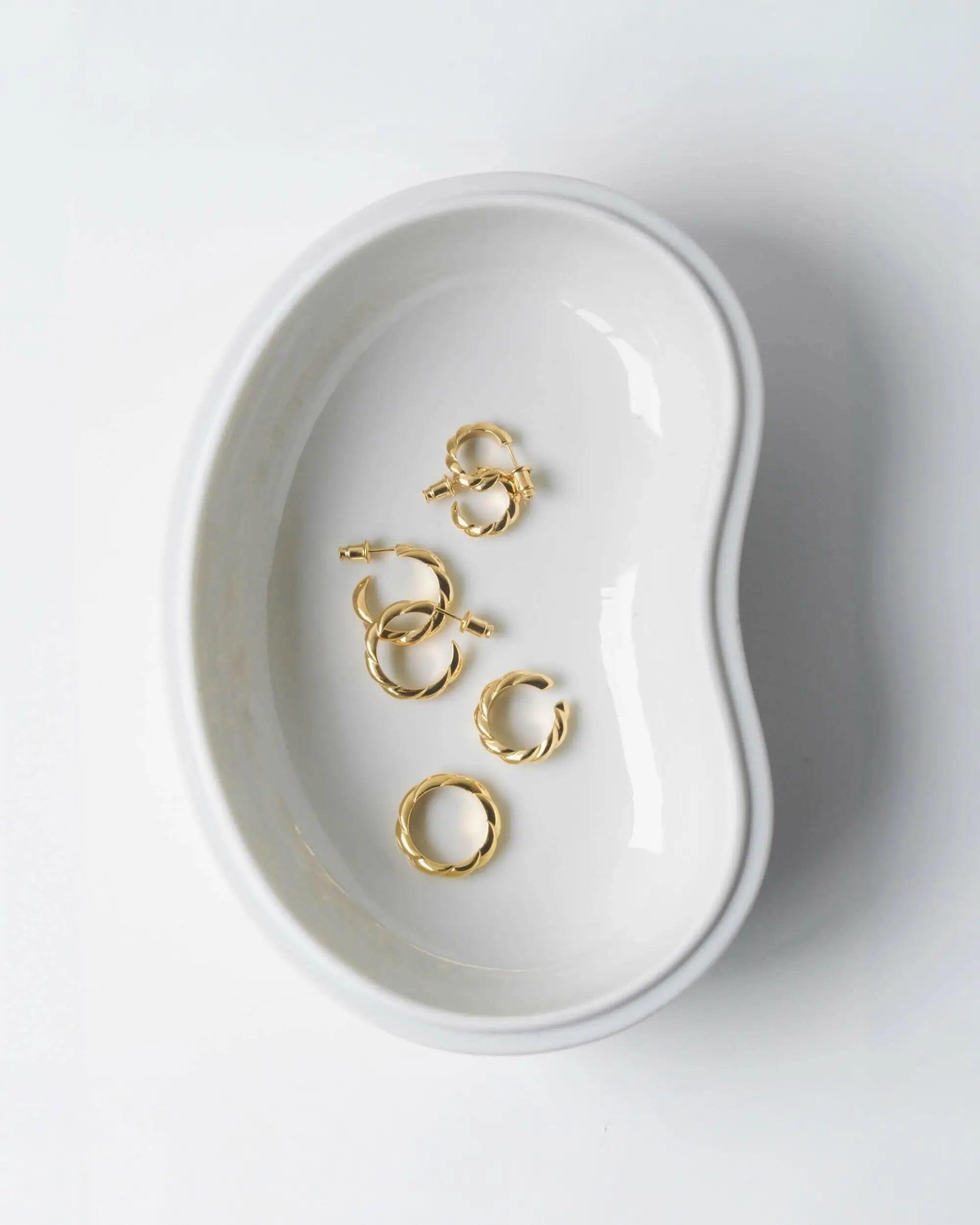 白いウェーブトレイに並べられたゴールドのイヤーカフコレクション。日常使いでも安心してご着用いただけるつけっぱなし対応のニッケルフリーアイテム。