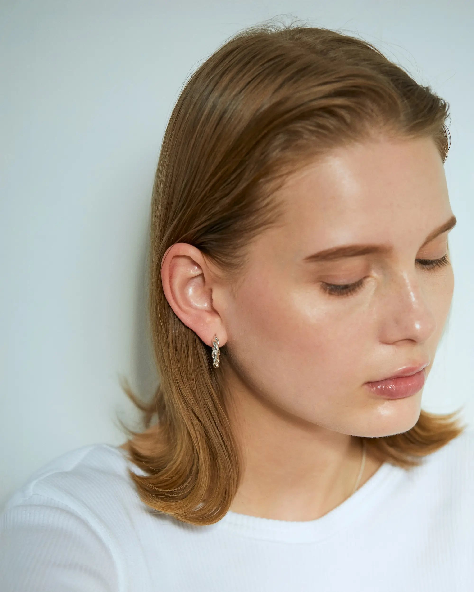 つけっぱなしにも対応するシルバー製のウェーブピアスを着用し、伏し目がちに佇む女性のエフォートレスな姿。