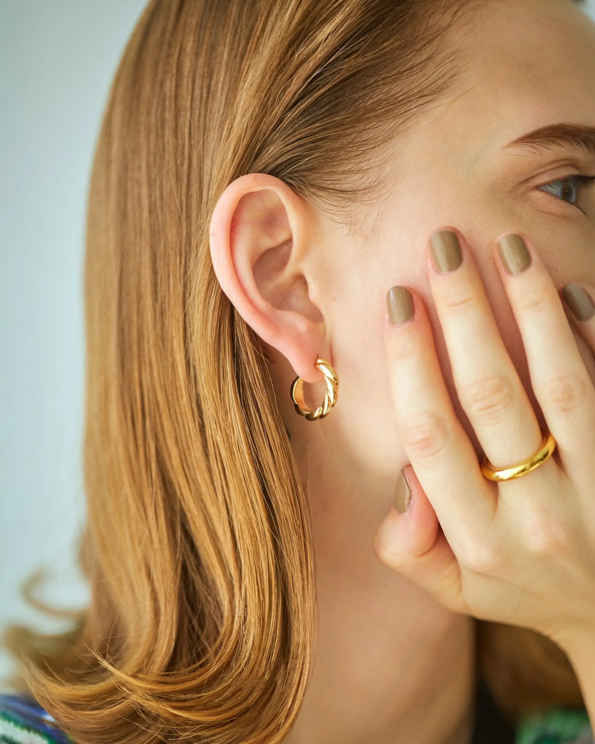 コーディネートに上品なアクセントを添える、ゴールドウェーブピアス(Mサイズ)を着用した耳元のクローズアップ。