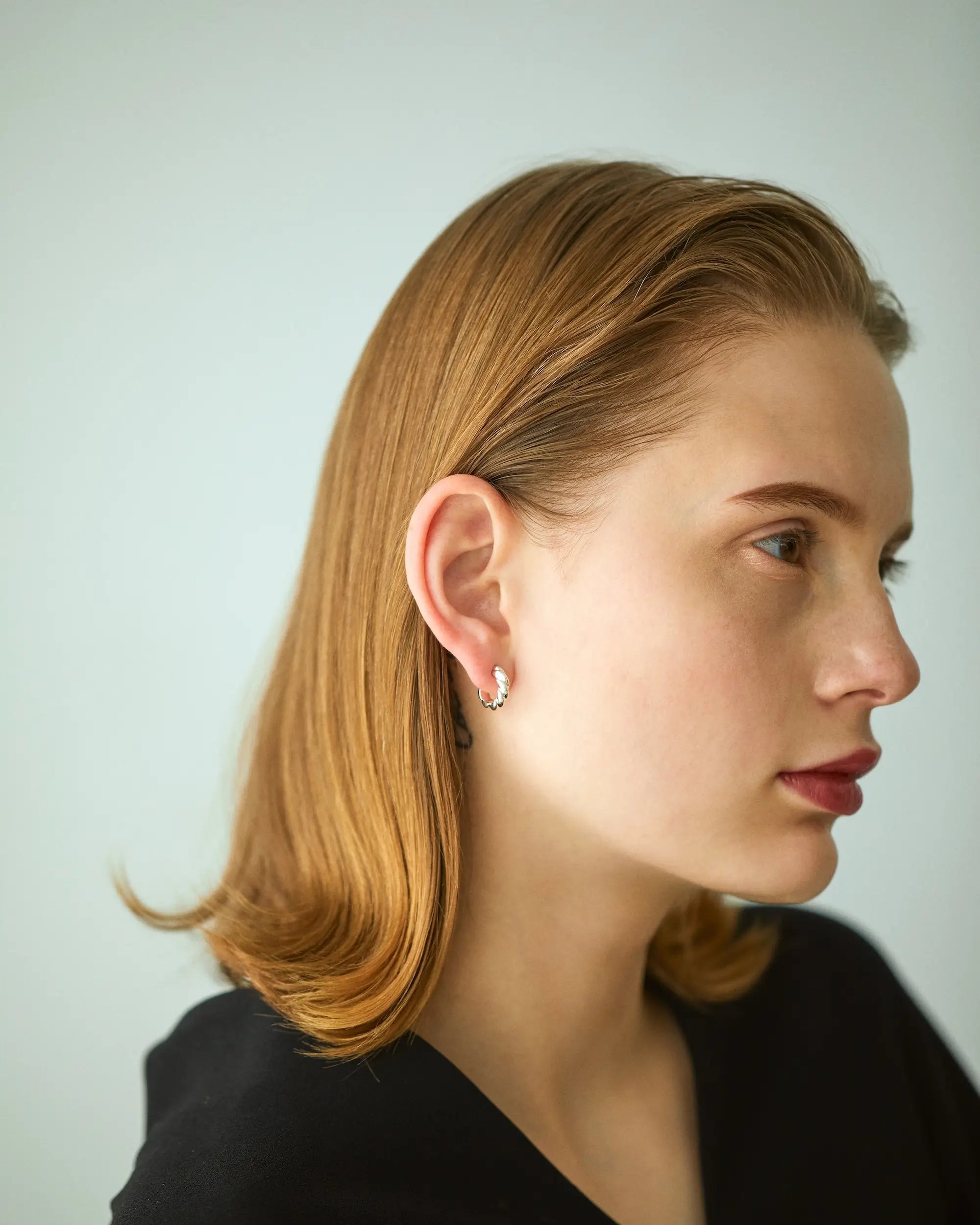 黒いトップスを着た女性モデルが、小ぶりなゴールドのウェーブピアスを右耳に着用している洗練された横顔のポートレート。