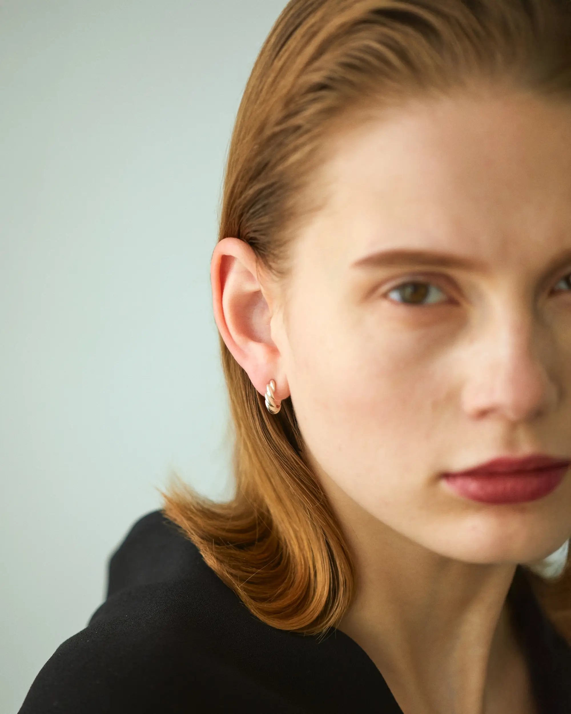 赤いリップの女性モデルが、ゴールドのウェーブフープピアスを着用して斜め前を見つめている着用イメージ画像。