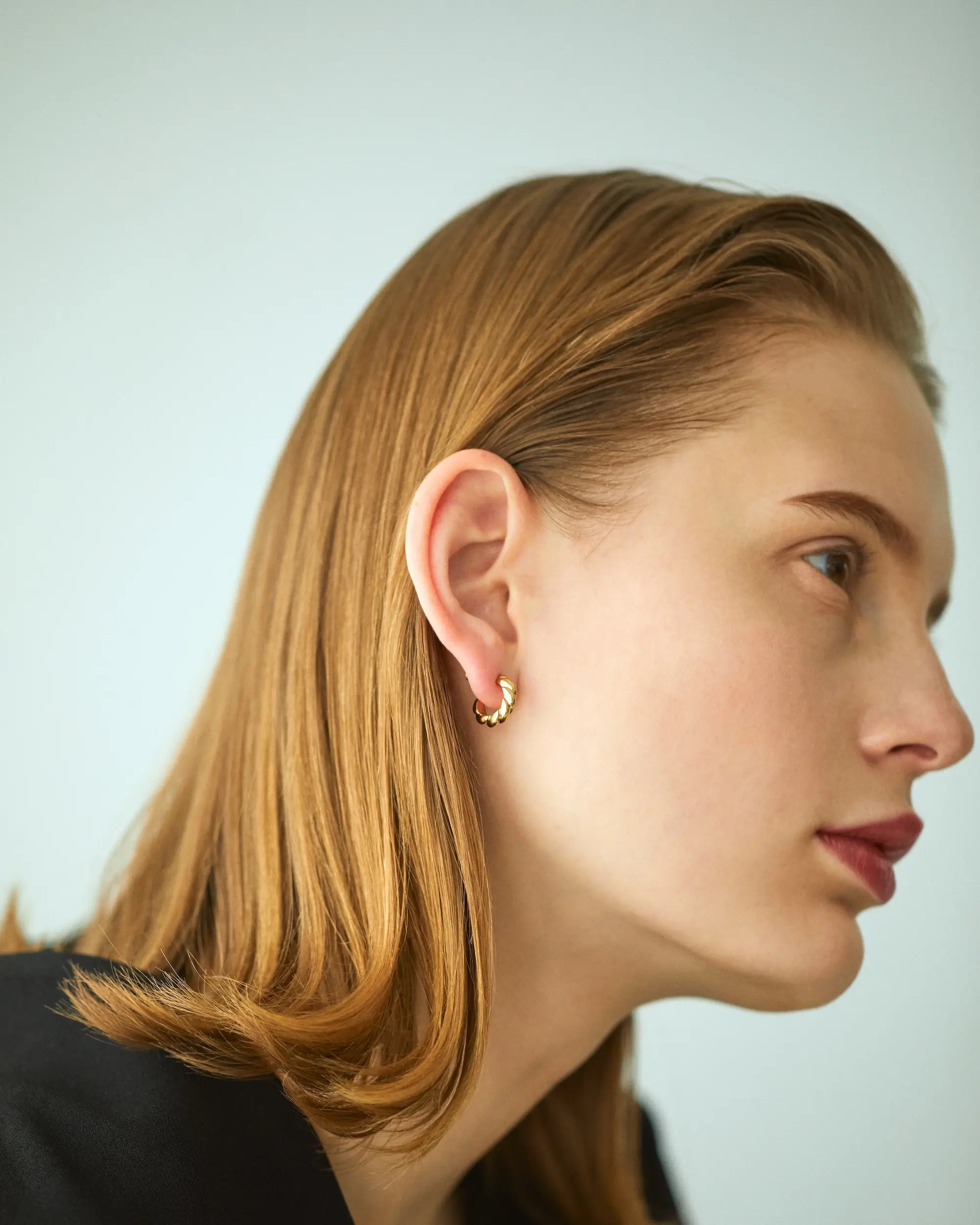 ゴールドのウェーブピアスを着用し、伏し目がちにうつむく女性モデルのエフォートレスな横顔。
