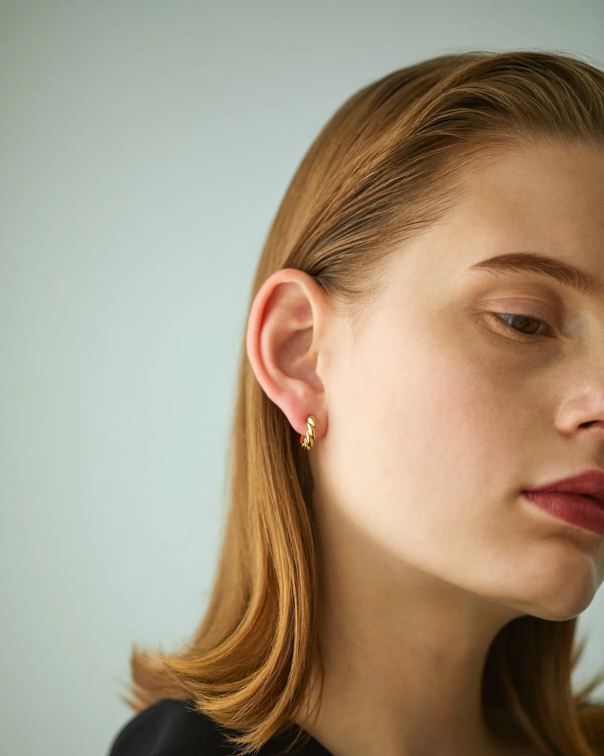 日常のコーディネートに上品に馴染む、小ぶりなウェーブピアスを着用した大人の女性の横顔ポートレート。