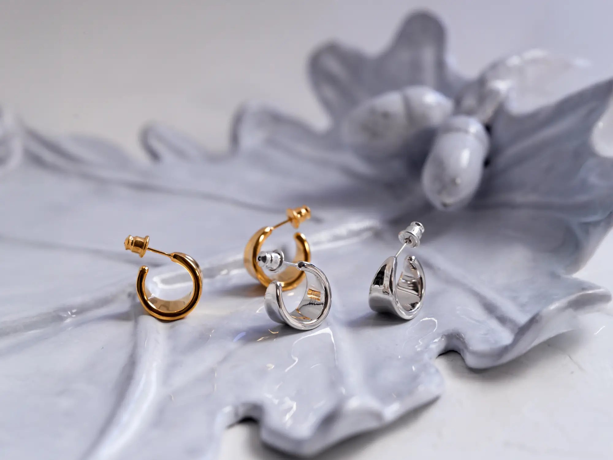 アンティーク調のグレーのリーフ型トレイに美しく並べられた、Aletta Jewelryのシルバー925とK10ゴールドのチャンキーフープピアス