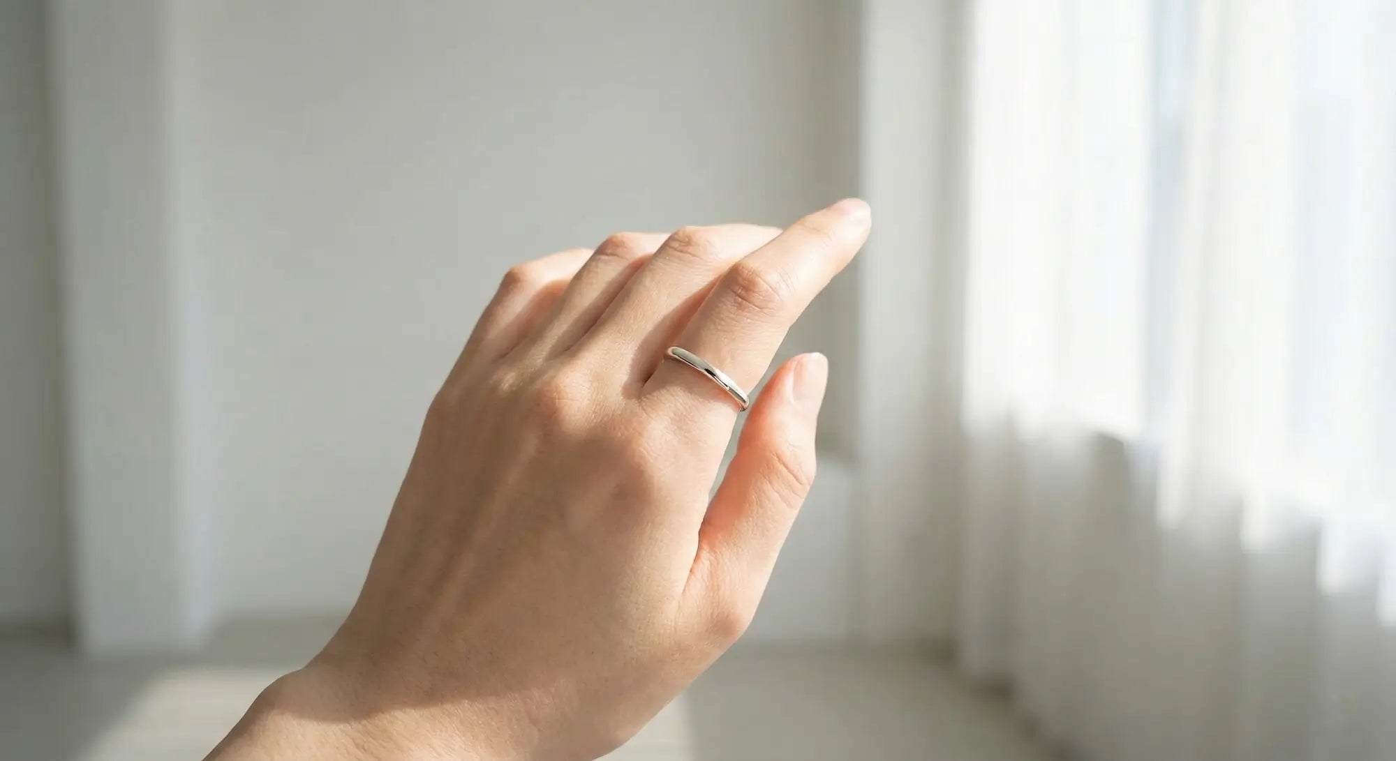 人差し指に着けられたシンプルなシルバーリングを眺める女性の手元