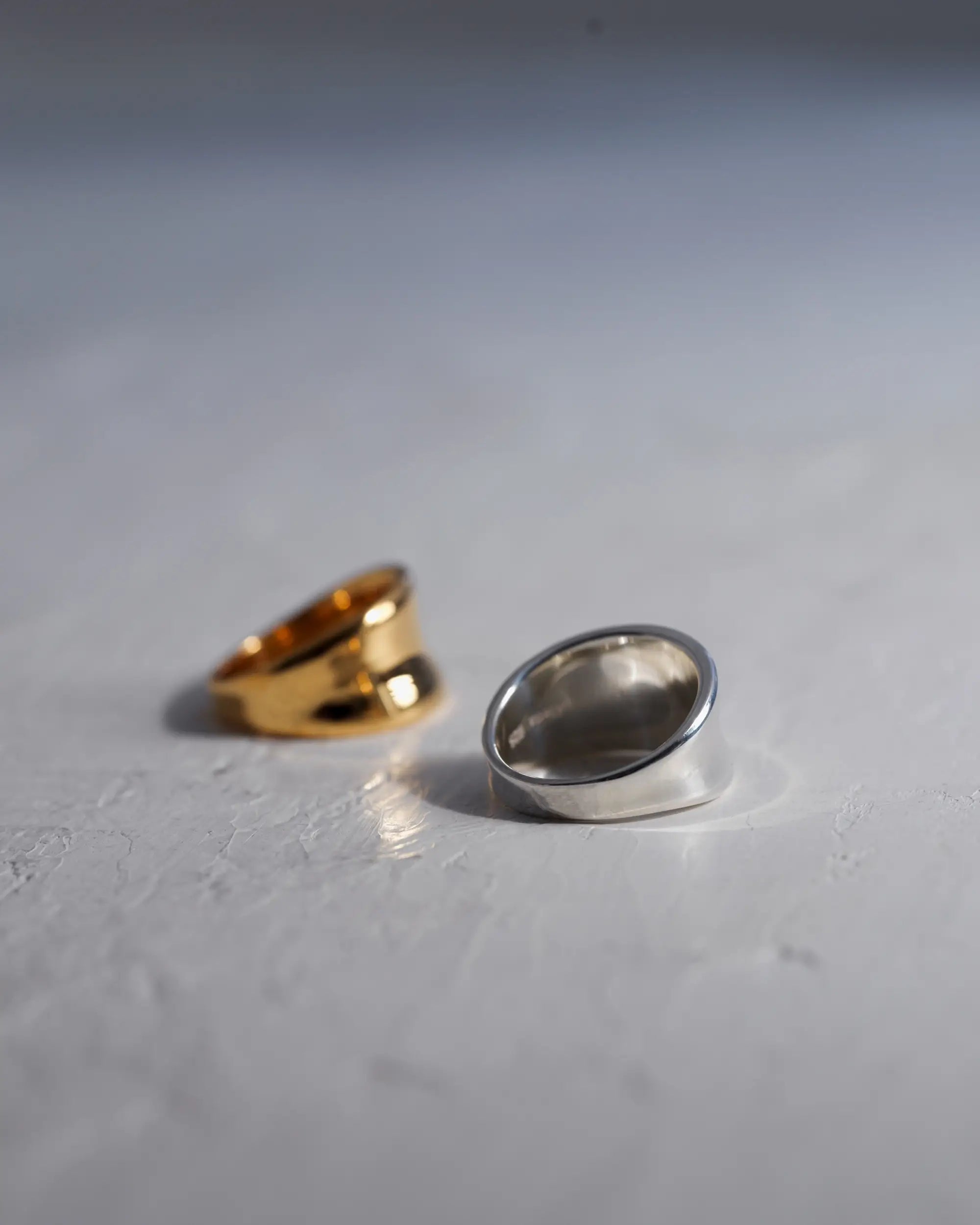 白いテクスチャのある背景に並ぶ、Botanical Ring（ボタニカルリング）のゴールドとシルバーのペアショット。