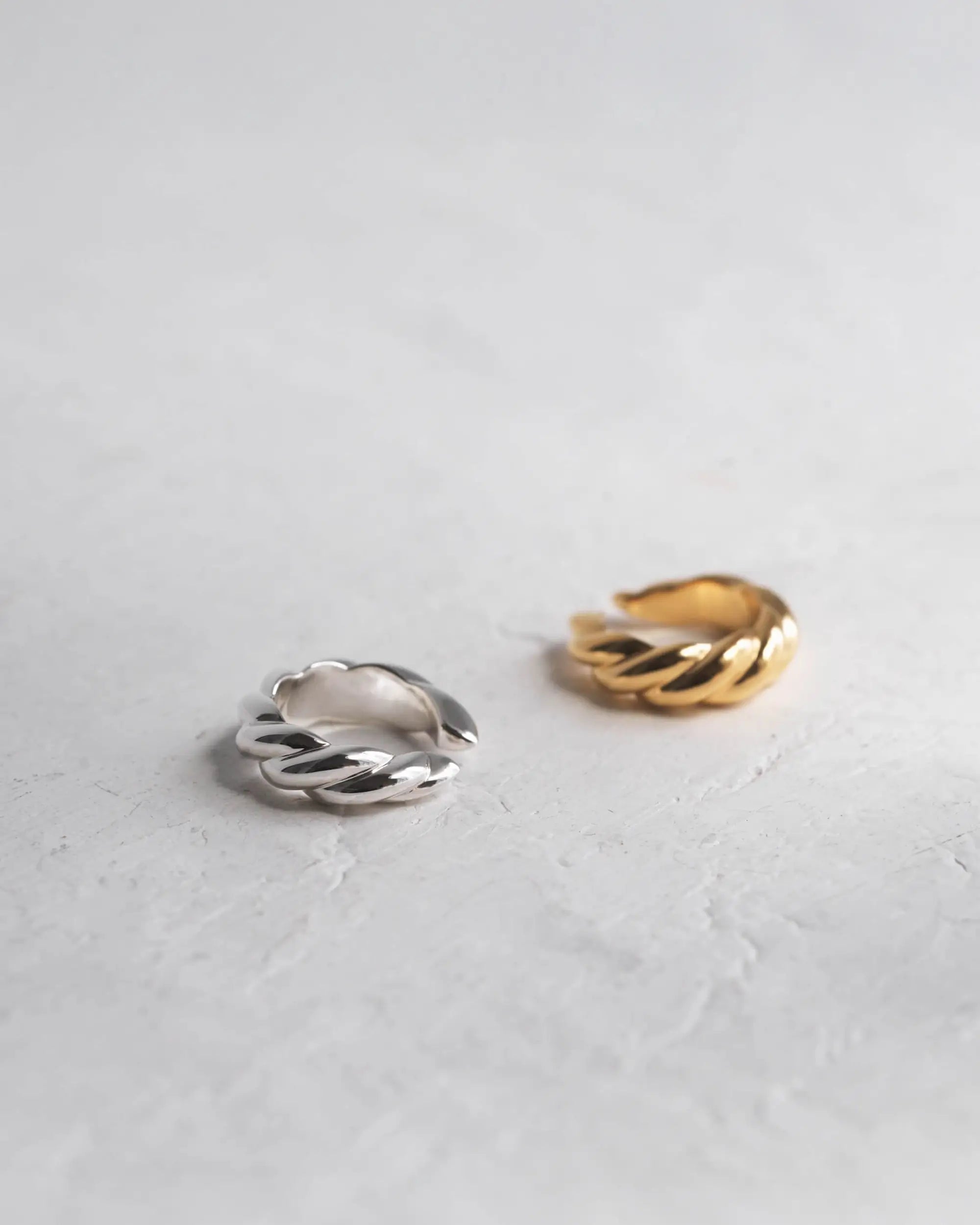 コンクリート背景に置かれたシルバーとゴールドのウェーブイヤーカフ。ピアスホール不要でつけっぱなしにできる金属アレルギー対応のSilver925素材。