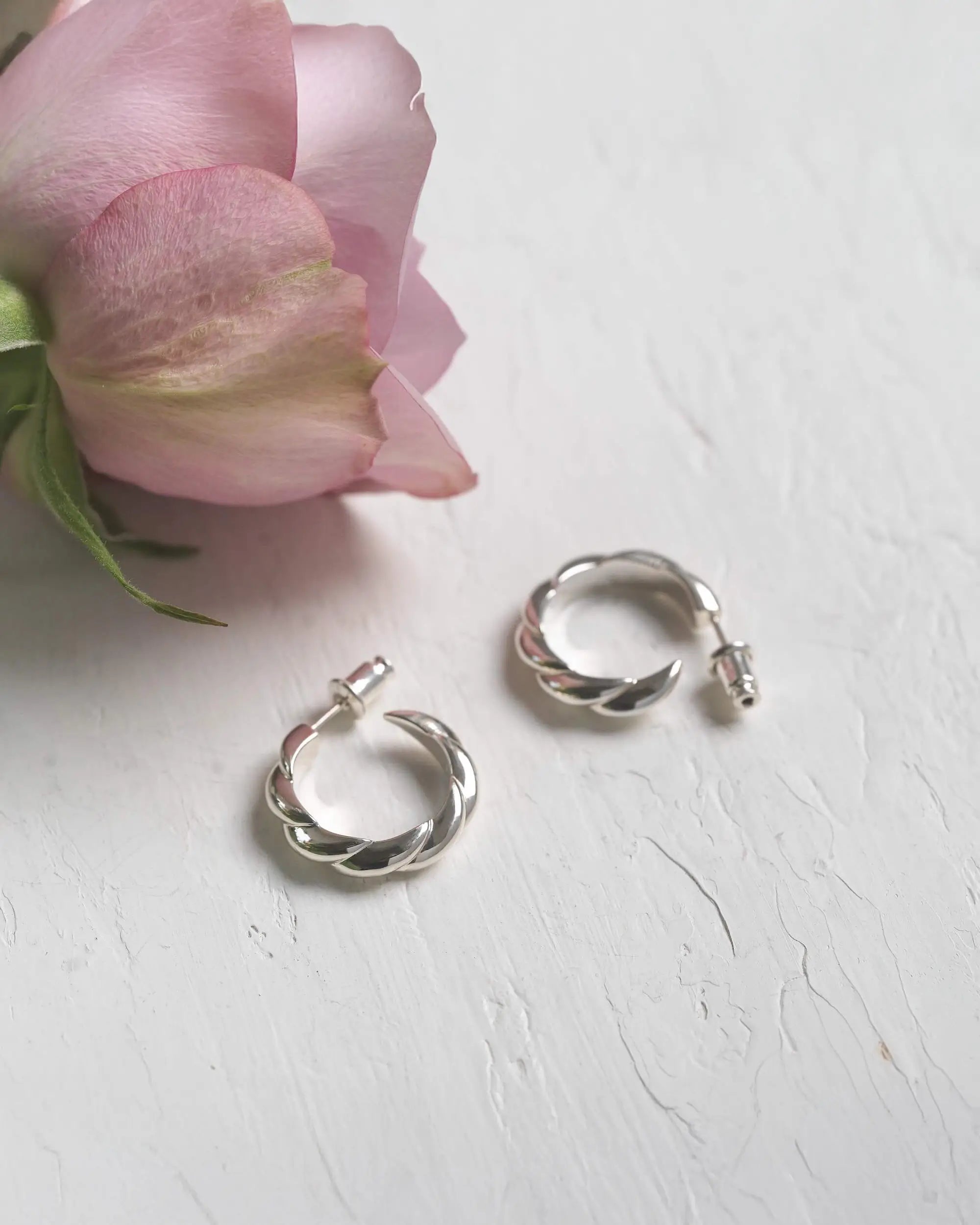 ピンクの薔薇と一緒に置かれた、シルバー925製の大ぶりなウェーブピアス（Mサイズ）。海面をモチーフにした立体的な曲線が美しい置き画。