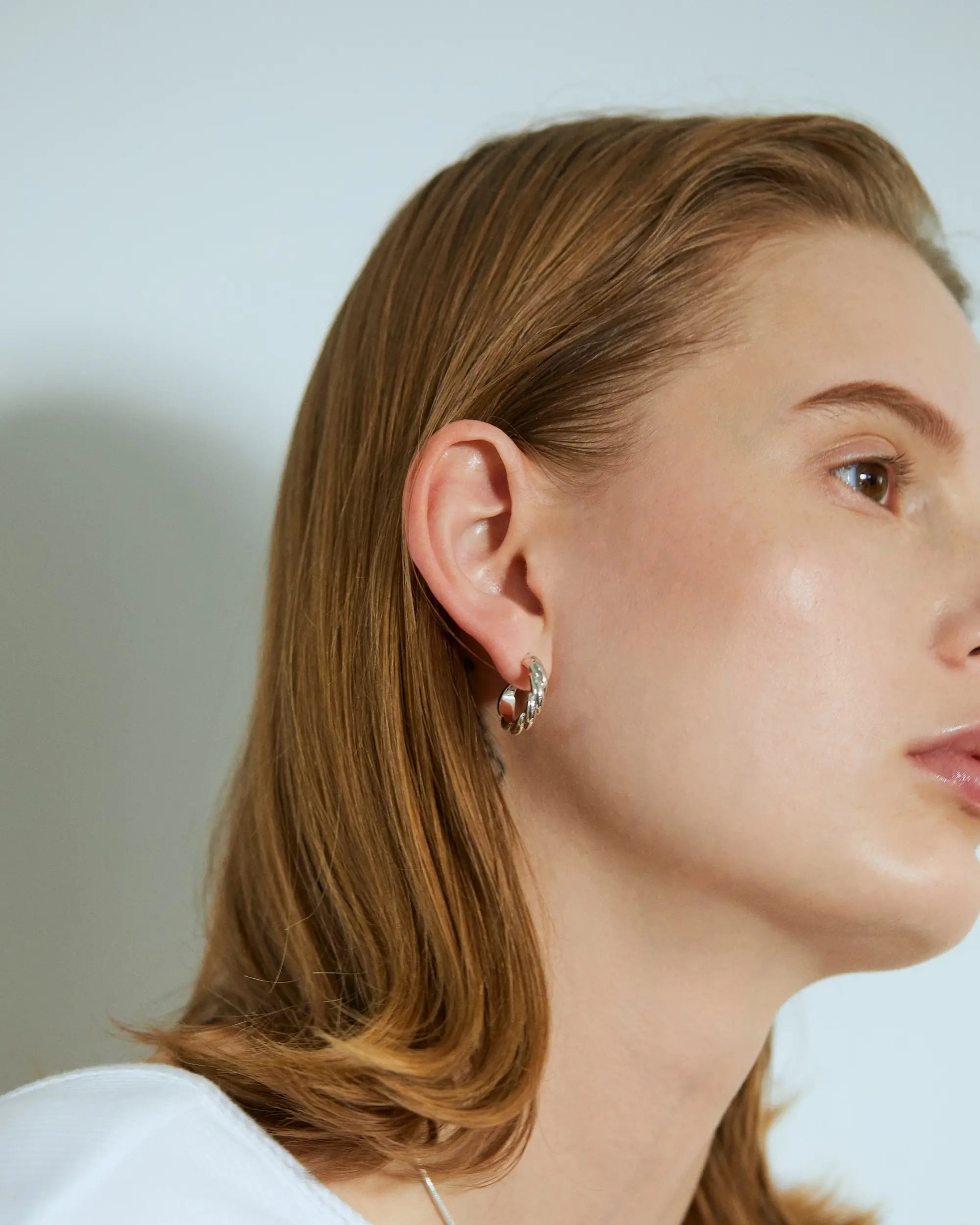 白いトップスを着た女性が、大ぶりなシルバーのウェーブフープピアスを着用している洗練された横顔のポートレート。