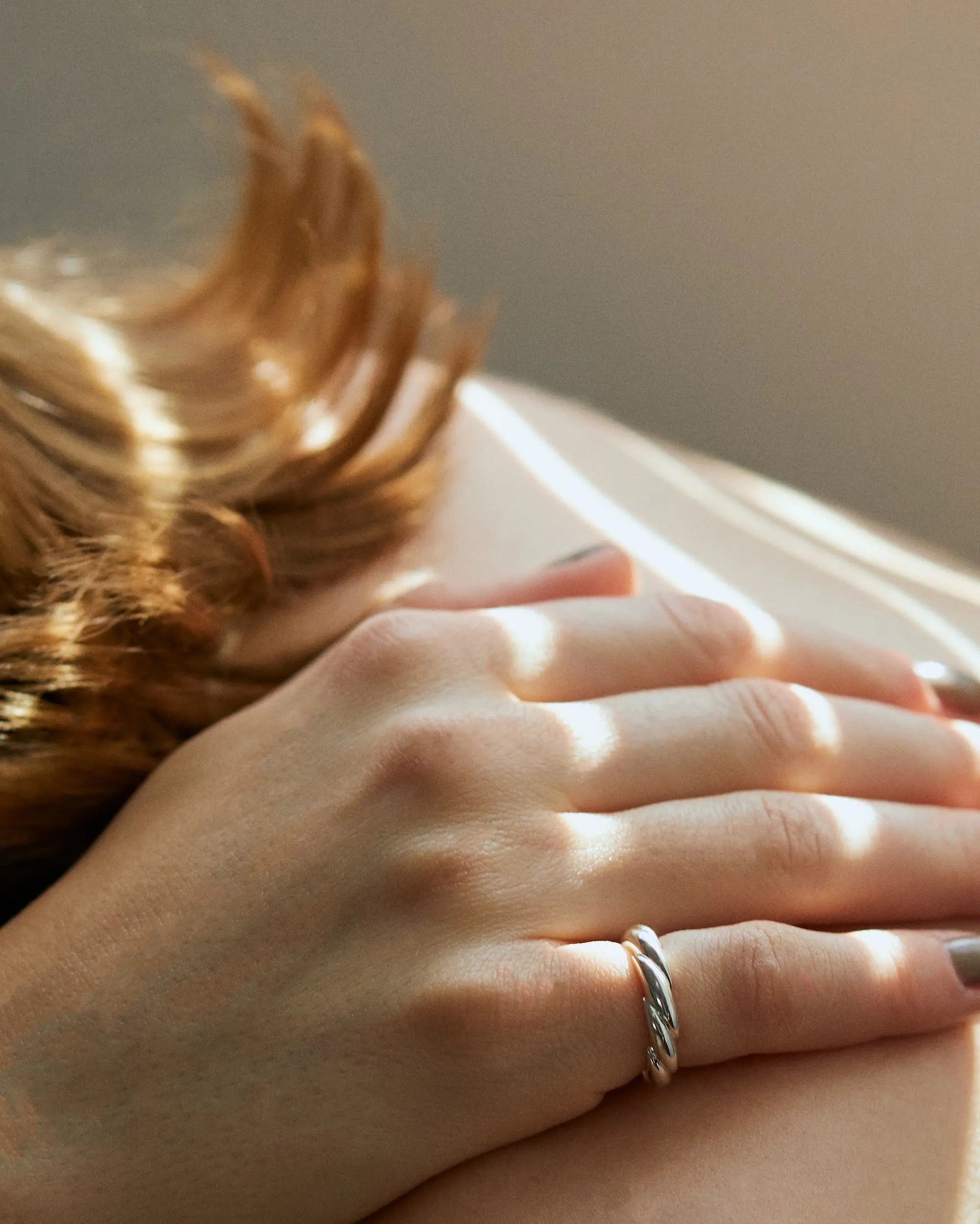 ブラインド越しの自然光が美しいウェーブリング（シルバー）の着用手元アップ。指を細く長く見せる計算されたカーブと、金属アレルギー対応のSilver925素材が特徴。